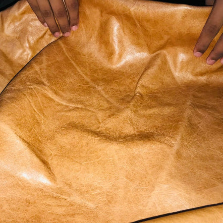 Brown leather fabric with hands holding it, showing texture and color.